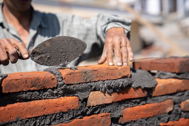 Bricklayer industrial worker installing brick masonry with trowel putty knife at construction site Premium Photo
