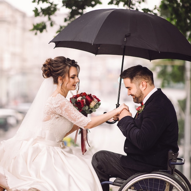 車椅子の花嫁と新郎は公園のベンチでキスをして座っている 無料の写真