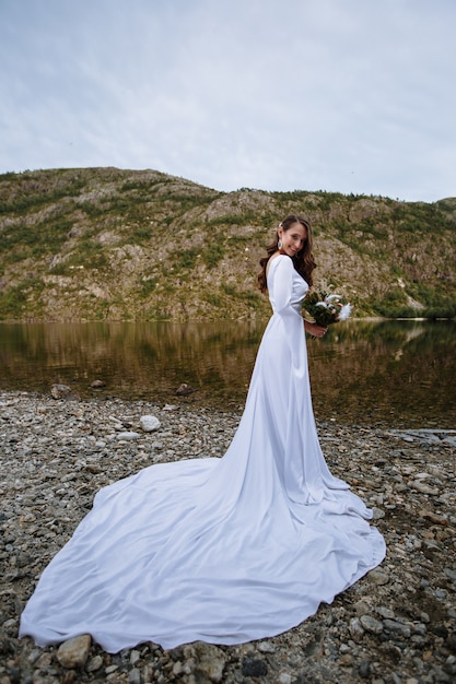 Premium Photo A Bride In A Long Wedding Dress Standing On The Shore Of A Lake 5851