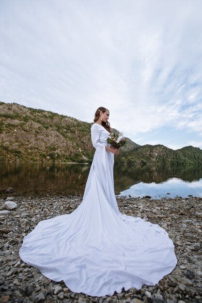 Premium Photo A Bride In A Long Wedding Dress Standing On The Shore Of A Lake 3568