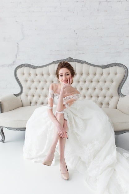 Bride looking out the window, she waits for the groom sitting on big classic sofa.  Free Photo