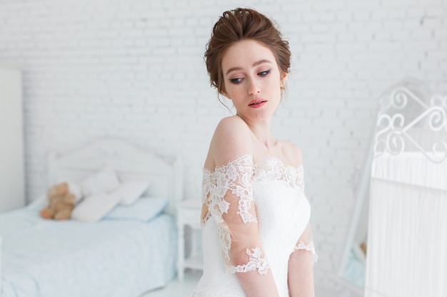 Bride posing in wedding dress in the studio on a background of a brick wall and white bed Free Photo