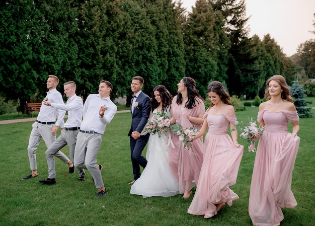 無料の写真 ピンクのドレスに身を包んだ花嫁介添人 最高の男性 結婚式のカップルが緑の庭を楽しそうに歩いています