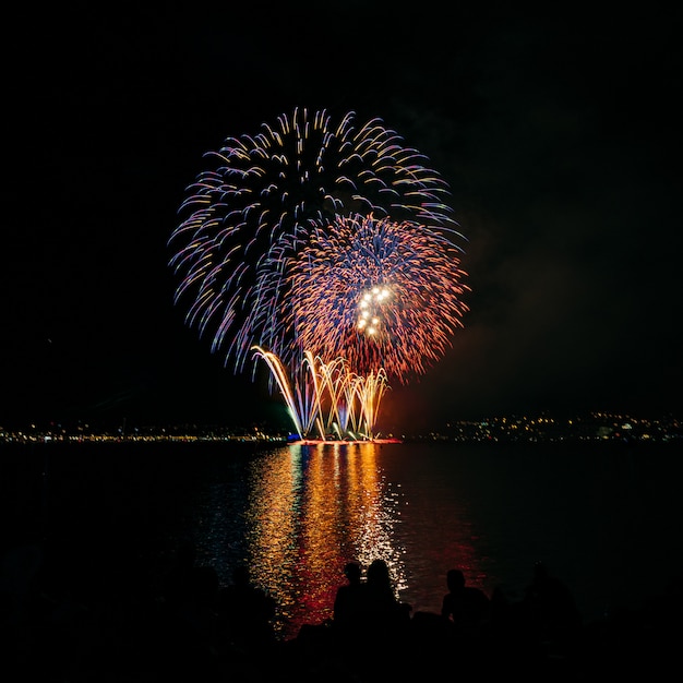 水の上の暗い夜空に明るい色の花火 プレミアム写真