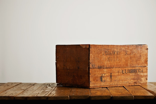 白い壁の背景に木製のテーブルにかろうじて判読可能な黒い文字と茶色の素朴な木製のワインボックス 無料の写真