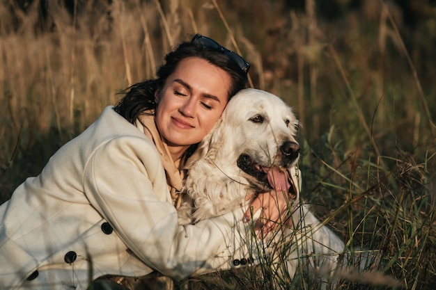 Premium Photo | Brunette girl hugging white golden retriever in the field