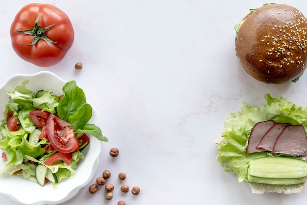 Burger; vegetable salad; whole tomato; hazelnut over white surface Free Photo