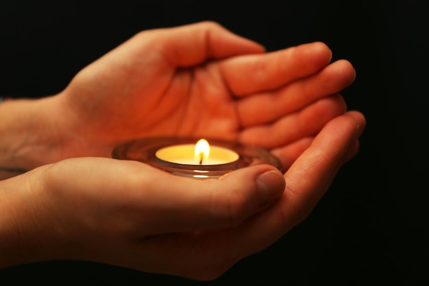 Premium Photo | Burning candle in hands on dark surface