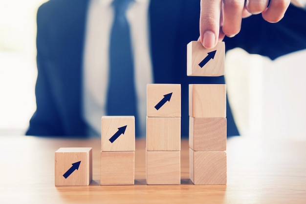 Business concept growth success process, close up businessman hand arranging wood cube with arrow stacking as step stair. Premium Photo