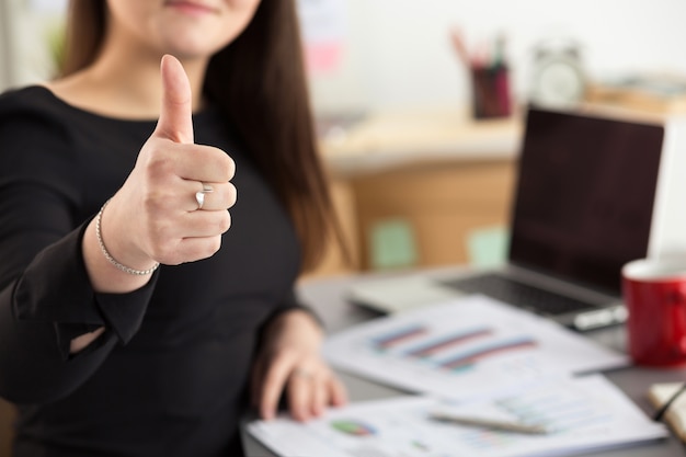 Business woman shows thumb up sitting at her office closeup. perfect goods or service quality concept Premium Photo