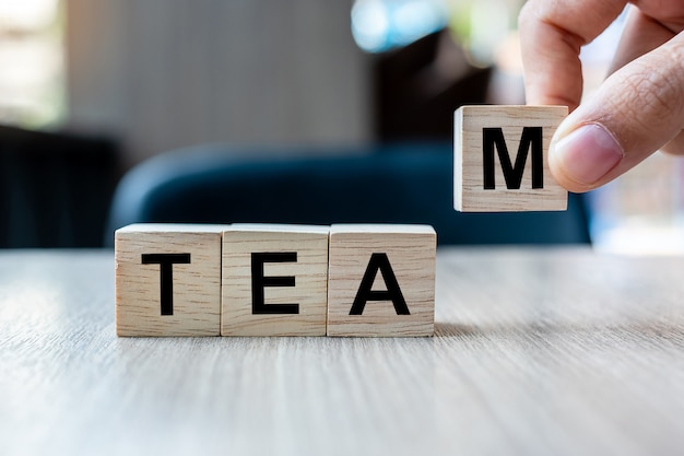 Businessman hand holding wooden cube block with team business word. cooperation, together, business and teamwork concept Premium Photo