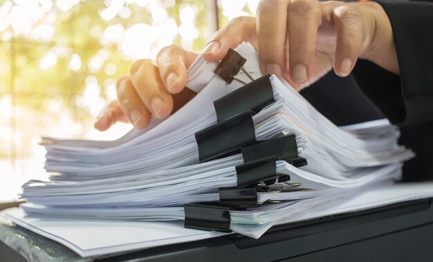 Businessman hands working in stacks of paper files for searching information on work desk office Premium Photo
