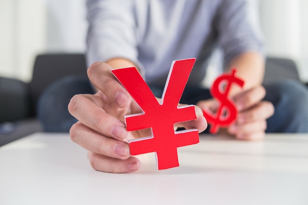 Businessman holding dollar sign and cny sign Free Photo