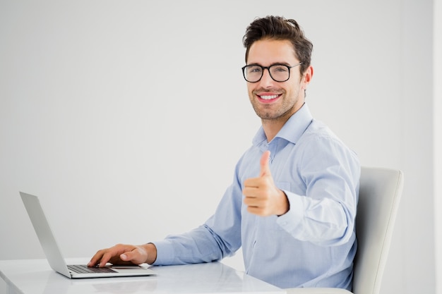 Businessman showing thumbs up while using laptop Premium Photo