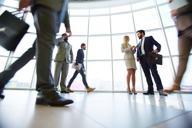 White collar workers communicating in office against window with their colleagues walking around.