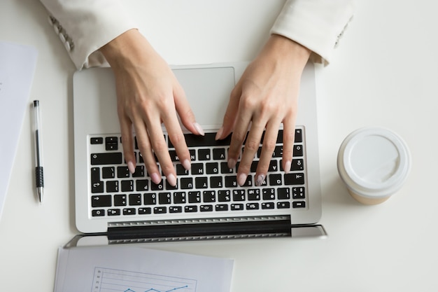 Businesswoman working on laptop, hands typing on keyboard, top view Free Photo