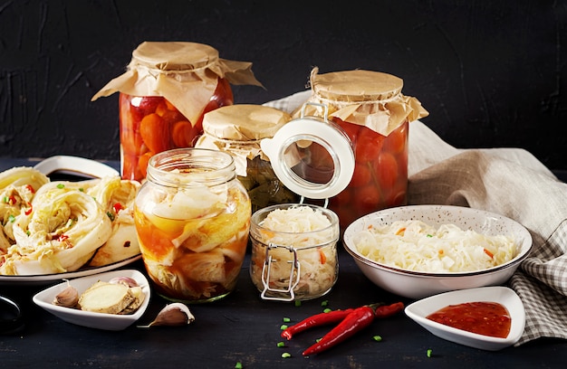 Cabbage kimchi, tomatoes marinated, sauerkraut sour glass jars over rustic kitchen table. Free Photo