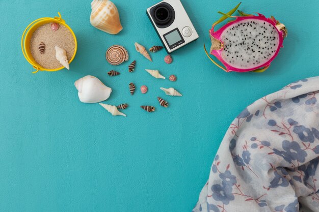 Camera, seashell, sand,beach pants,dragon fruit and smartphone over blue Premium Photo