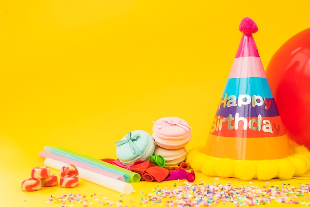 candies-straw-deflated-balloon-macarons-paper-hat-yellow-background_23-2147890014.jpg