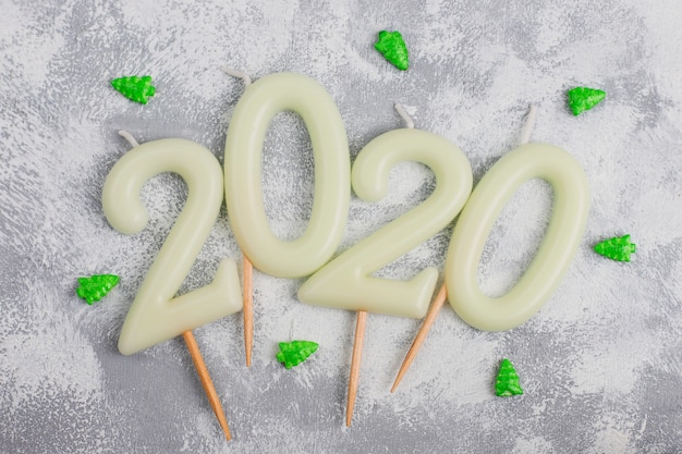 Candles in the shape of numbers 2020 as a symbol of the new year next to christmas shaped sparkle candies on a gray table. top view, flat lay Free Photo