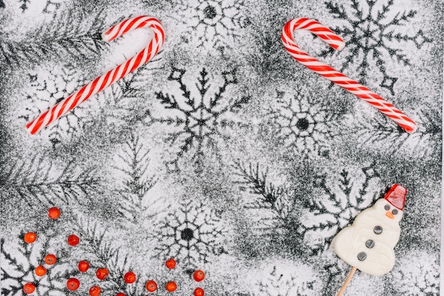 Candy canes and snowman lollipop on powdered sugar Free Photo