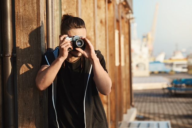 人生のあらゆる瞬間をとらえる ビンテージカメラを通して見る若いスタイリッシュな写真家の屋外ショット 港 ヨット 海岸のショットを撮って フリーの カメラマンとして働いています 無料の写真