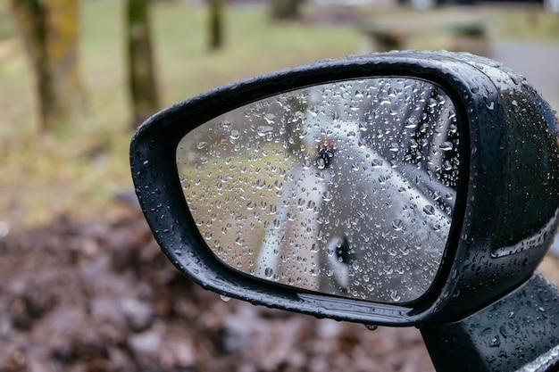 悪天候で運転している道路の雨の日のぼやけた背景に雨滴が付いている車のサイドミラー プレミアム写真