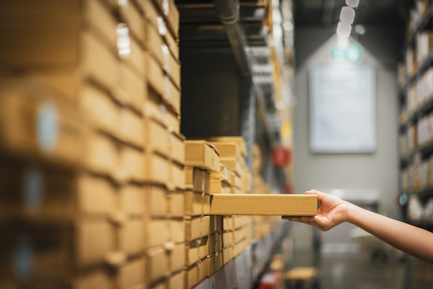 Cardboard box package with blur hand of shopper woman picking product from shelf in warehouse. Premium Photo