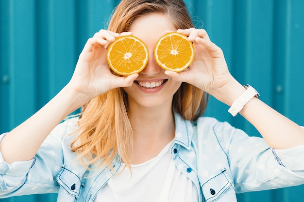 Carefree young beautiful girl using two halfs on oranges instead of glasses over her eyes Free Photo