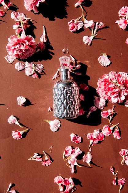 茶色の表面にカーネーションの花びらと香水瓶 プレミアム写真