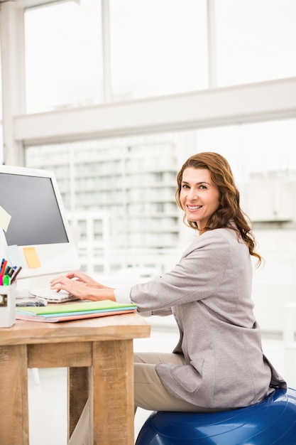 Casual Businesswoman Sitting On Exercise Ball While Working Photo