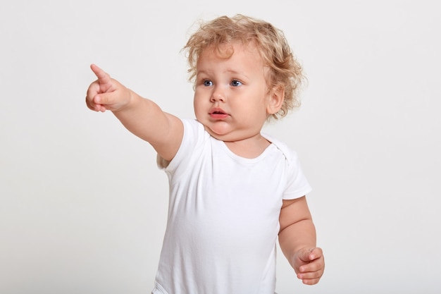 人差し指で指さしている白人の赤ちゃん Tシャツを着て何か面白いものを見る プレミアム写真