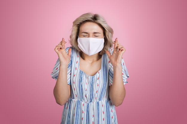 Premium Photo Charming Blonde Lady In Summer Dress With Medical Mask On Face Gesturing A Dream On A Pink Wall