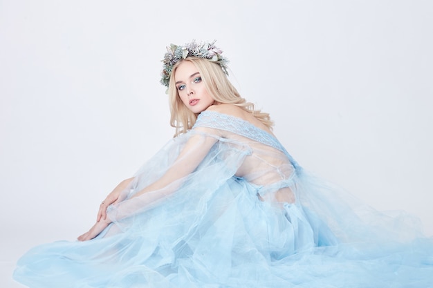 青い空気のようなドレスと白い背景の上の頭に花輪を着た魅力的な妖精の女性 完璧な肌とメイクの優しい神秘的なブロンドの女の子 清潔さ ボディケア 肌 プレミアム写真