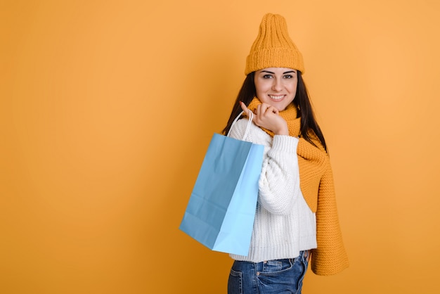 Charming girl in knitted hat and scarf with shopping bags posing in studio Premium Photo