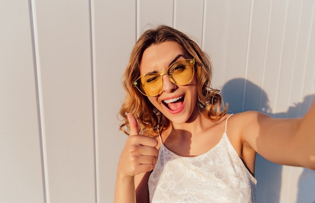 Charming smiling girl in yellow eyeglasses winking and showing a thumb up  Free Photo