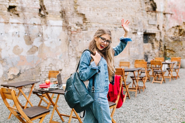 Charming student passed exams perfectly. adorable girl in a fashionable denim suit leaves the outdoor cafe and says goodbye to friends. Free Photo