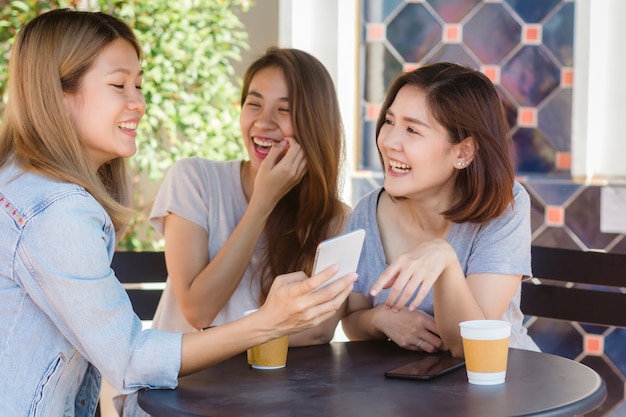 Cheerful asian young women sitting in cafe drinking coffee with friends and talking together Free Photo