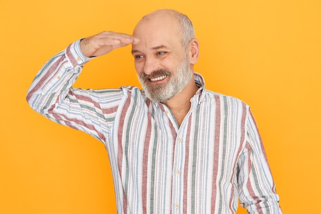 Free Photo Cheerful Attractive Elderly Male With Gray Beard And Bald Head Posing Isolated Keeping Hand Over His Eyes To Protect Himself