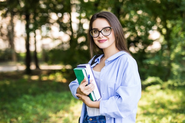 Cheerful attractive young woman with books standing and smiling in park Free Photo