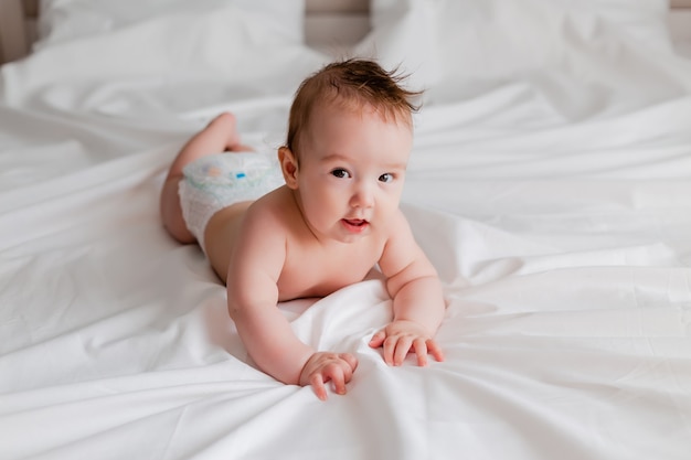 Premium Photo | Cheerful baby is lying on his stomach on a white bed