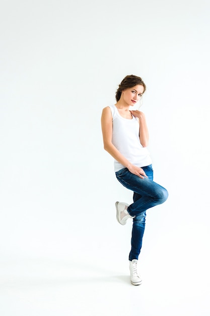 Premium Photo Cheerful Girl In A White T Shirt And Dark Blue Jeans In The Studio On A White Background Stands Sits Runs