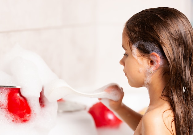 Premium Photo Cheerful Little Caucasian Girl Plays With Foam While Bathing In The Bathtub 