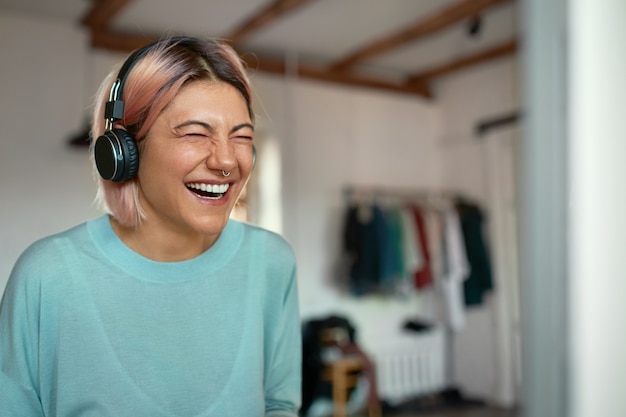 Cheerful positive young female blogger with nose ring laughing while recording podcast, using headset. Free Photo