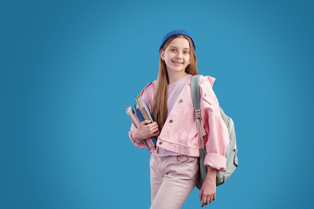 Premium Photo Cheerful Teenage Student In Pink Denim Jacket Beanie And Jeans Holding Stack Of Books By Chest While Standing In Front Of Camera