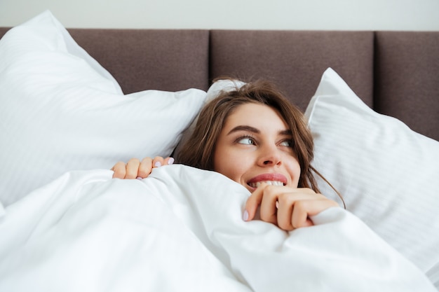 Free Photo | Cheerful young lady lies in bed at home under a blanket.