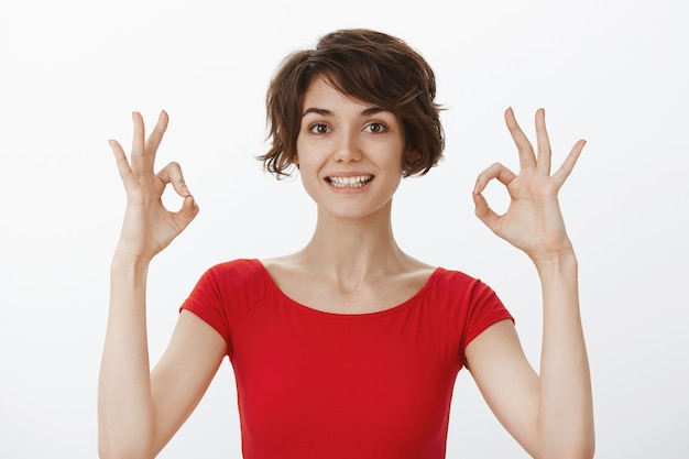 Cheerful young woman guarantee perfect quality, recommend product, showing okay gesture Free Photo