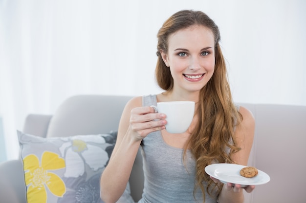 Premium Photo Cheerful Young Woman Sitting On Sofa Holding Cup And Saucer 