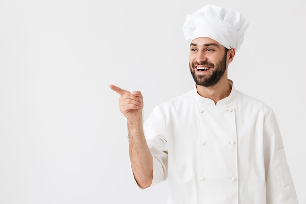 Premium Photo | Cheery optimistic young chef posing in uniform pointing ...