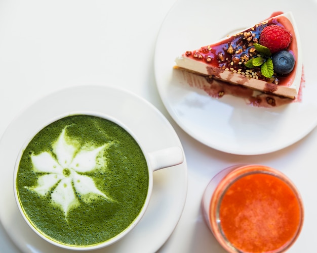 Cheesecake with berries; smoothie and cup of matcha latte art on white background Free Photo